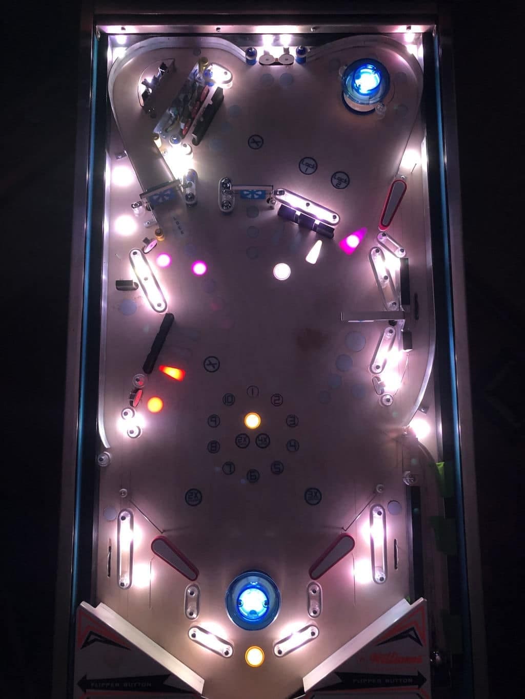 Illuminated pinball machine playfield with colorful lights and bumpers at night